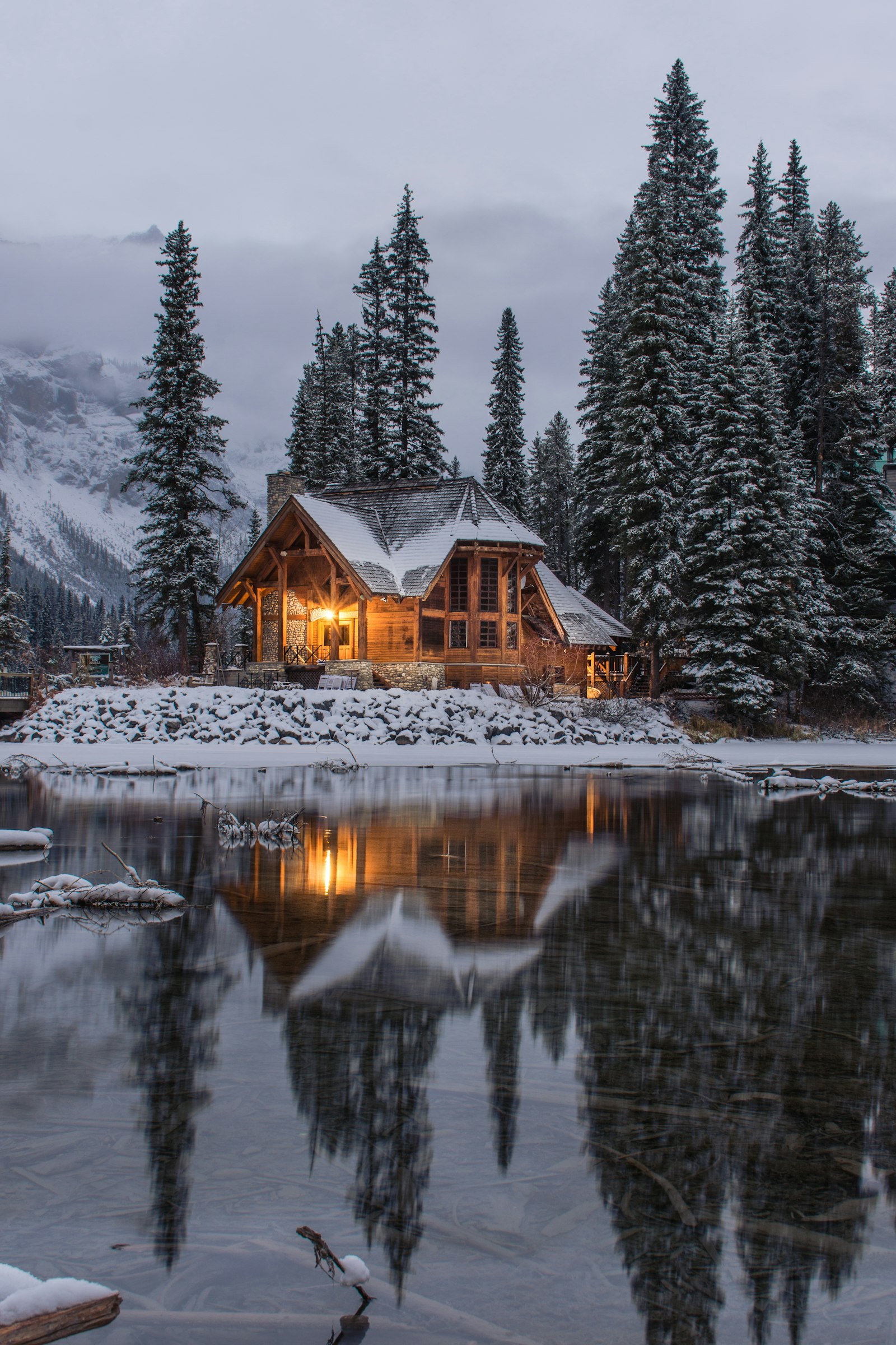 A warmly lit cabin in snow by still water